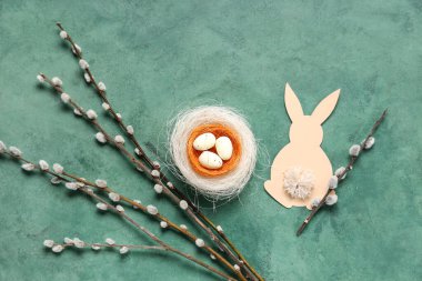 Nest with Easter eggs, pussy willow branches and paper bunny on green background