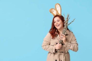 Beautiful young woman in bunny ears with pussy willow branches on blue background. Easter celebration