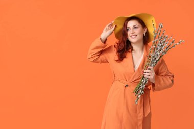 Beautiful young woman with pussy willow branches on orange background. Easter celebration