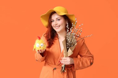 Beautiful young woman with pussy willow branches and toy chick on orange background. Easter celebration