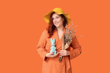 Beautiful young woman with pussy willow branches and toy bunny on orange background. Easter celebration