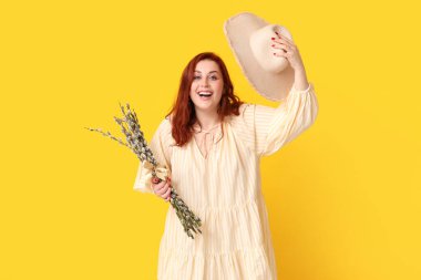 Beautiful young woman with pussy willow branches and hat on yellow background. Easter celebration