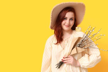 Beautiful young woman with pussy willow branches and chick on yellow background. Easter celebration