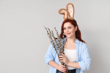 Beautiful young woman in bunny ears with pussy willow branches on grey background. Easter celebration