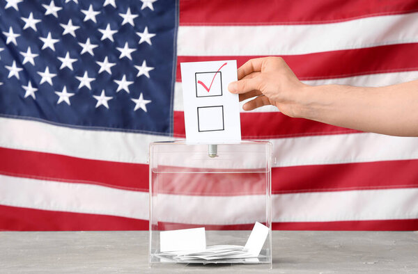 Голосование у избирательного ящика на столе против флага США