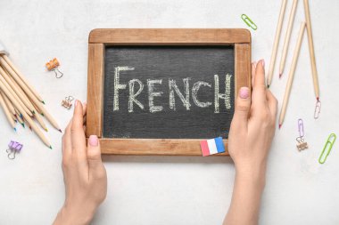 Kadın eli, yazı tahtası FRENCH ve arka planda kırtasiye malzemesi, yakın plan.