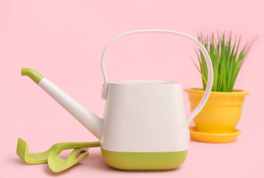 Bahçe aletleri ve pembe arka planda çimen olan teneke kutu sulama.