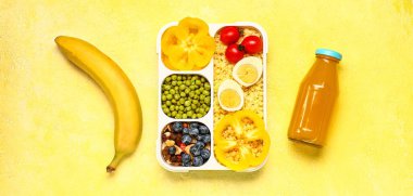 İçinde lezzetli yemekler ve sarı arka planda bir şişe meyve suyu olan beslenme çantası.