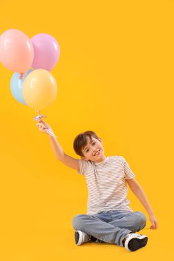 Sarı arka planda oturan balonlu küçük çocuk. Çocuk Bayramı kutlaması