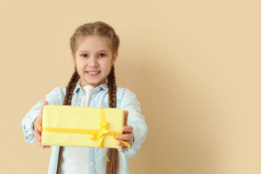 Bej arka planda hediye kutusu olan küçük bir kız. Çocuk Bayramı kutlaması