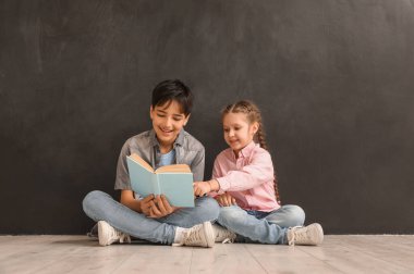 Küçük çocuklar tahtanın yanında kitap okuyor.