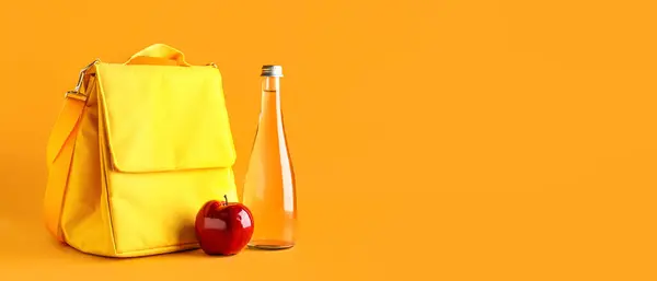 Lunch box bag with apple and bottle of water on orange background with space for text