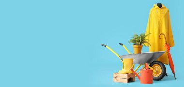 Mavi arka planda bitki, yağmurluk ve bahçe malzemeleri ve metin için yeri olan el arabası.