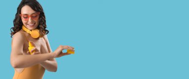 Açık mavi arkaplan üzerine güneş kremi sürerken mutlu genç kadın metin için boşluk bırakıyor