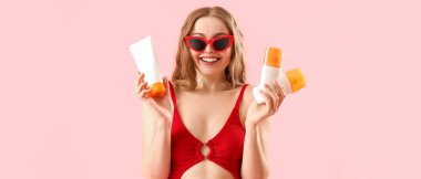 Pembe arka planda güneş kremleri olan mutlu genç bir kadın.  