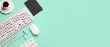 Bilgisayar fareli kablosuz klavye, kulaklıklar, bir fincan kahve ve turkuaz arka planda ofis kırtasiyesi.