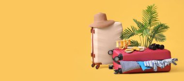 Plaj aksesuarlı bavullar ve sarı arka planda giysiler ve metin için yer.