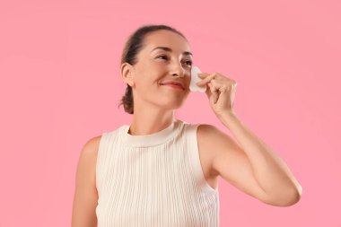 Güzel olgun kadın Guasha 'yı pembe arka planda yüz masajı için kullanıyor.