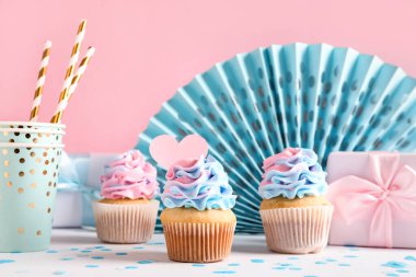 Pembe arka planda hediye kutuları ve süslemeleri olan lezzetli kekler. Cinsiyet ortaya çıkan parti kavramı