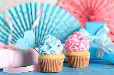 Soru işaretli lezzetli kekler, hediye kutuları ve beyaz arka planda mavi ahşap masa üzerindeki süslemeler. Cinsiyet ortaya çıkan parti kavramı