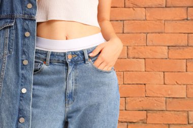 Turuncu tuğla duvarın yanında şık kot elbiseli genç bir kadın.