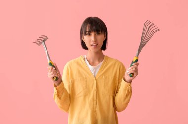 Pembe arka planda bahçe tırmıkları olan güzel bir kadın bahçıvan.