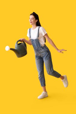 Sarı arka planda sulama tenekesi olan güzel, genç, mutlu bir bahçıvan.