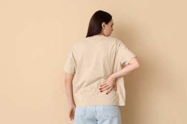 Bej arka planda sırt ağrısı çeken genç bir kadın.