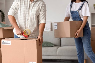 Happy young couple taping box in room on moving day clipart