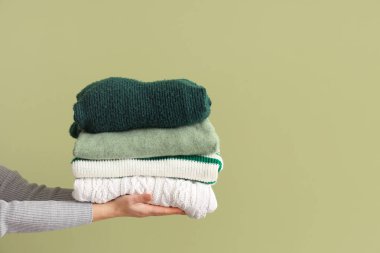 Yeşil arka planda katlanmış kazaklı bir kadın.