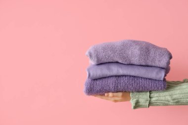 Pembe arka planda katlanmış kazaklı bir kadın.