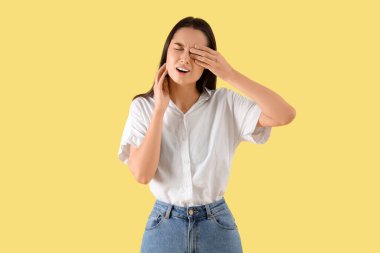 Sarı arka planda diş ağrısı çeken genç bir kadın.