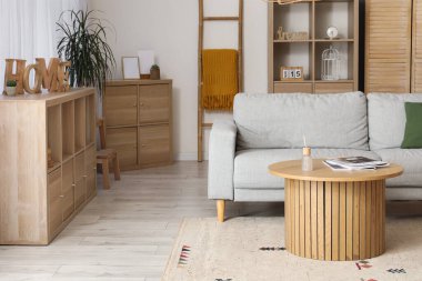 Gri kanepesi, ahşap masası ve çekmeceleri olan rahat bir oturma odası.