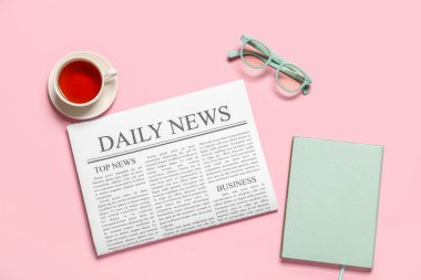 Gözlüklü gazete, not defteri ve pembe arka planda bir fincan çay.