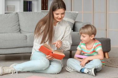 Küçük çocuk ve annesi evde oturmuş kitap okuyorlar.