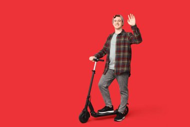 Kırmızı arka planda modern elektrikli scooter kullanan genç bir adam.