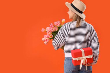 İşitme cihazlı genç bir kadın elinde lale ve turuncu arka planda hediye tutuyor. Uluslararası Kadınlar Günü
