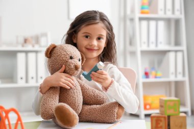 Çocuk kliniğinde oyuncak ayı ve astım spreyi olan küçük bir kız.
