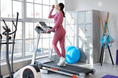 Spor salonundaki koşu bandında astım spreyi kullanan genç bir kadın.