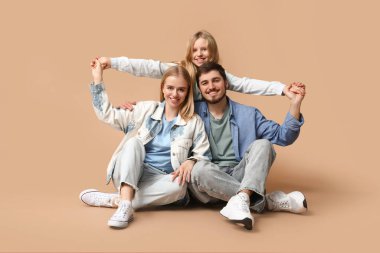 Kahverengi arka planda oturan şık kot elbiseli mutlu bir aile.