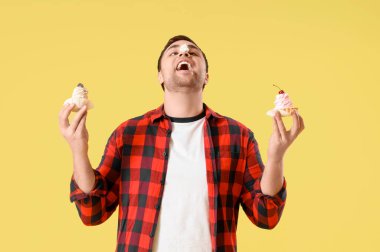 Burnunda krema ve sarı arka planda pastalar olan genç bir adam. Aşırı yeme kavramı