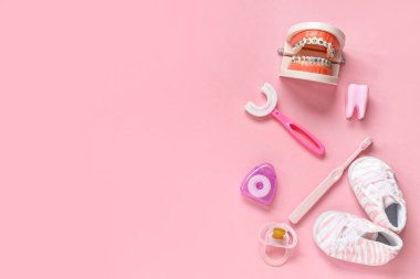 Pembe zemin üzerinde çene modeli, ayakkabı ve emzik ile çocuk diş fırçaları