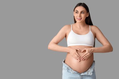 Genç hamile bir kadın hafif arka planda kalp hareketi yapıyor.