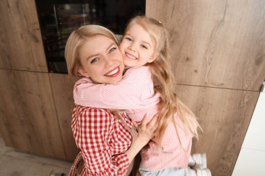 Evde fırında elmalı turta pişirirken annesiyle sarılan küçük kız.