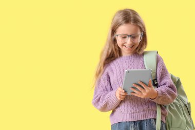 Sarı arka planda tablet bilgisayar kullanan gözlüklü şirin bir kız.