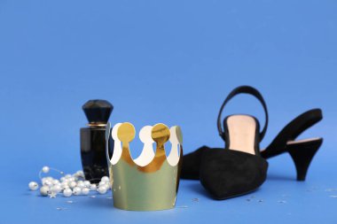 Şık topuklu kağıt taç, kolye ve mavi arka planda bir şişe parfüm. Balo konsepti