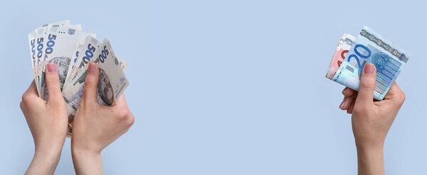 Hands with hryvnia and euro banknotes on light blue background