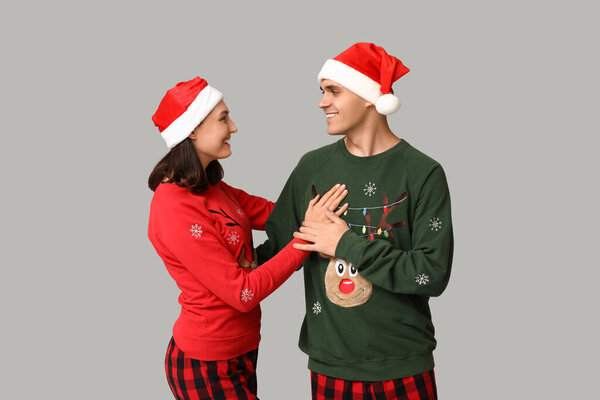 Happy young couple in Christmas pajamas and Santa hats on grey background