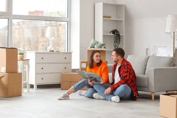 Happy young couple reading interior design magazine in room on moving day