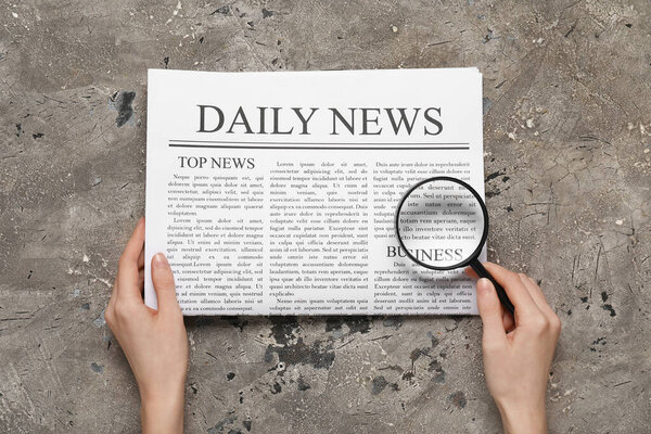 Руки женщины с газетой и увеличительным стеклом на сером фоне гранжа